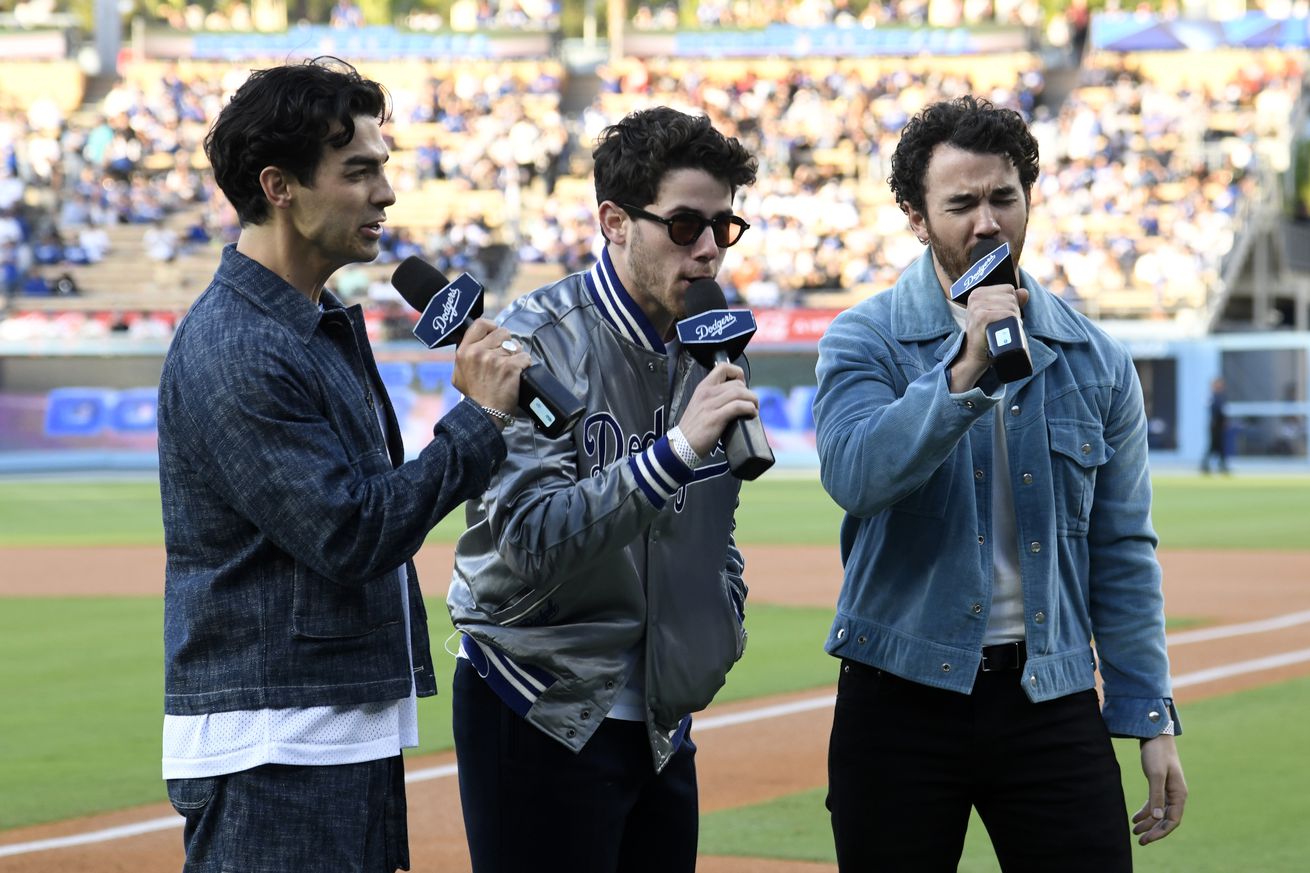 LOS ANGELES, CALIFORNIA - JUNE 23: From left, Joe Jonas , Nick Jonas and Kevin Jonas, of the Jonas Brothers announce to the fans “It’s time for Dodger baseball!” before the start of the game between the Los Angeles Dodgers and Houston Astros at Dodger Stadium on June 23, 2023 in Los Angeles, California.
